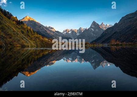 Bergspiegelung auf dem See. Schöne Landschaft mit hohen Bergen mit beleuchteten Gipfeln und blauem Himmel. Landschaftlich Schöner Blick Auf Den See Und Die Berge Stockfoto