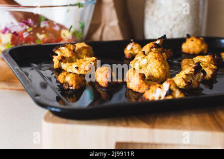 Lifestyle-Bild von hausgemachten Tandoori gerösteten Blumenkohl auf einem Backblech mit einer Schüssel Salsa im Hintergrund Stockfoto
