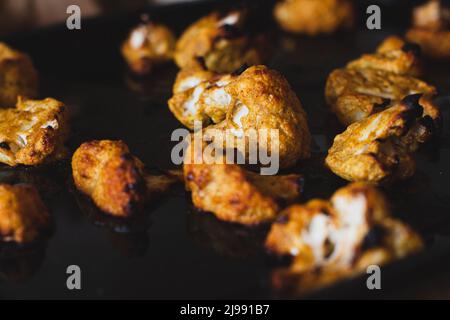 Dunkles und Moody Food Bild von Tandoori geröstetem Bio-Blumenkohl auf einem Backblech. Stockfoto