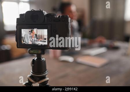 Nahaufnahme der Videoaufnahme einer jungen Frau mit Kopfhörern, die am Tisch sitzt und Inhalte für den Blog erstellt Stockfoto