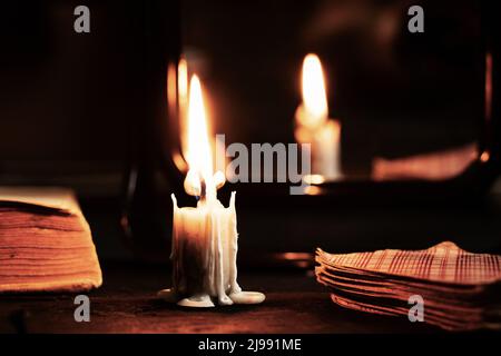 Eine brennende Kerze wurde von Spiegeln getragen und Wahrsagerkarten liegen in der Nähe, Wahrsagerei auf Karten bei Kerzenlicht auf einem schwarzen Tisch, Magie, Hexe A Stockfoto