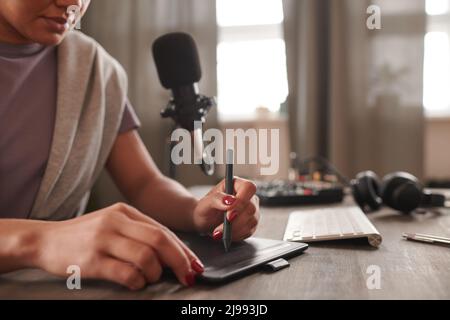 Mittlere Nahaufnahme einer nicht erkennbaren digitalen Künstlerin, die am Schreibtisch sitzt und mit einem grafischen Pad etwas zeichnet Stockfoto