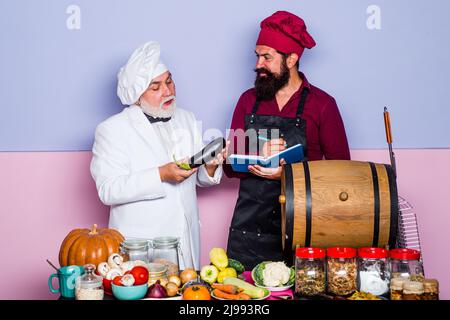 Zwei lächelnde Köche, Köche oder Bäcker. Bärtiger Koch, der in der Küche des Restaurants steht. Rezept kochen. Stockfoto