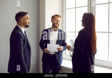 Geschäftskollegen in formellen Anzügen unterhalten sich während der Büropause angenehm. Stockfoto