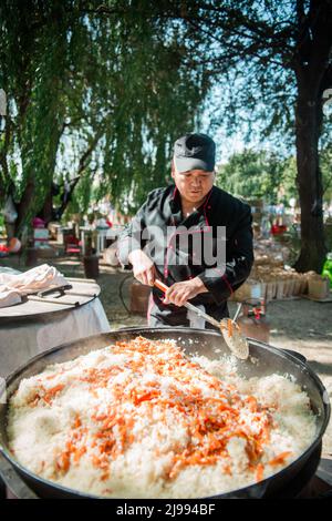 Ein männlicher Koch kocht Pilaf in einem großen Kessel auf der Straße. Stockfoto