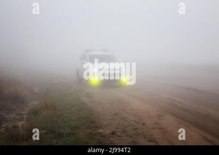 Weißes SUV-Auto mit gelben Nebelscheinwerfern auf einer Bergstraße im dichten Nebel Stockfoto