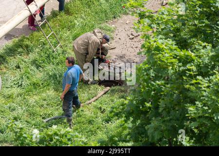 Tiraspol, Moldawien - 17. Mai 2022: Männliche Arbeiter beheben einen Bruch in einer Wasserversorgung und Kanalisationsleitung. Unfall auf der Linie der städtischen Infrastruktur. Mangelhafte q Stockfoto