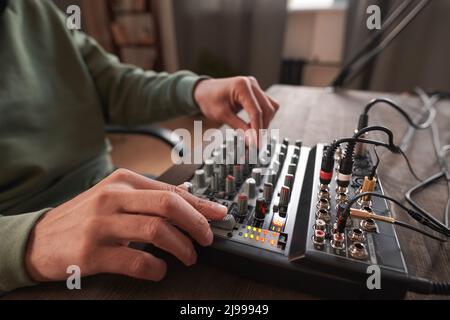 Mittlere Nahaufnahme von nicht erkennbaren Händen junger menschen, die den Audiomischer anpassen und den Sound im Heimstudio einstellen Stockfoto