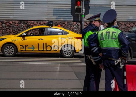 Moskau, Russland. 21.. Mai 2022. Ein Uber-Taxi fährt eine Straße im Zentrum von Moskau entlang, vor dem Hintergrund zweier Verkehrspolizisten, Russland Stockfoto