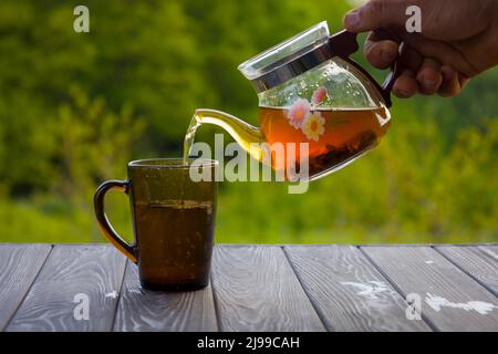 Tee in Glasbecher auf Holztisch auf unscharfem Hintergrund gießen, Stockfoto