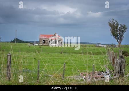 Verlassenes Haus auf dem Feld jenseits von Zaun und grünem Gras Stockfoto