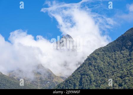 Hollyford River Valley zwischen Bergen und Gipfeln mit niedriger Wolke gegen blauen Himmel in Südinsel Neuseeland. Stockfoto