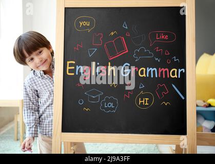 Netter kleiner Junge in der Nähe der Tafel mit Text ENGLISCHE GRAMMATIK Stockfoto