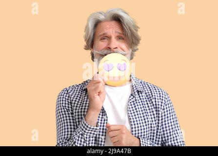 Älterer Mann mit fröhlichem Emoticon und herzförmigen Augen auf farbigem Hintergrund Stockfoto