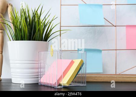 Verschiedene leere Haftnotizen, Zimmerpflanzen und Stimmungstafel auf dunklem Tisch in der Nähe einer weißen Wand Stockfoto