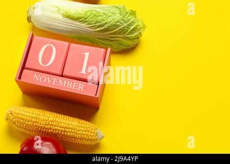 Gemüse- und Würfelkalender mit Datum NOVEMBER 1 auf gelbem Hintergrund, Nahaufnahme. Konzept des Welt-Vegan-Tages Stockfoto