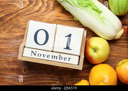 Frisches Gemüse, Obst und Würfelkalender mit Datum NOVEMBER 1 auf Holzhintergrund, Nahaufnahme. Konzept des Welt-Vegan-Tages Stockfoto