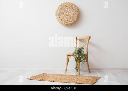 Korb mit Büchern und Zimmerpflanzen auf Stuhl in der Nähe der hellen Wand Stockfoto