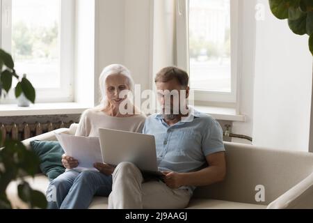 Konzentriertes, pensioniertes reifes Paar, das gemeinsam Papierdokumente prüft Stockfoto