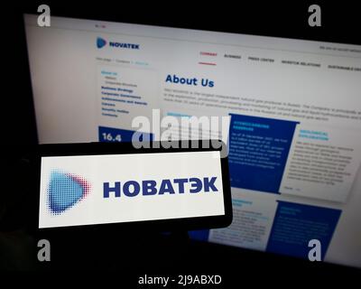 Person, die Mobiltelefon mit dem Logo des russischen Erdgasunternehmens Novatek auf dem Bildschirm vor der Business-Webseite hält. Konzentrieren Sie sich auf die Telefonanzeige. Stockfoto