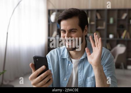 Happy Millennial man winken Hand hallo Blick auf Smartphone-Bildschirm Stockfoto