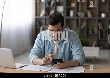 Seriöse junge Mann zählen auf Rechner prüfen Finanzinformationen Stockfoto