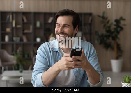 Fröhlicher, zwangloser junger Mann, der das Smartphone in der Ferne hält Stockfoto