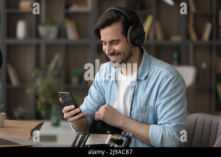 Millennial Mann Musiker im Headset halten Gitarre Telefonanruf machen Stockfoto