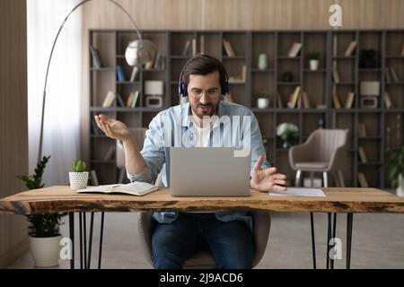 Selbstbewusster männlicher Lehrer im Headset gibt Videounterricht mit einem Laptop Stockfoto