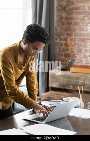 Nachdenkliche Afrikanerin, die sich über den Schreibtisch lehne und auf einem Laptop arbeite Stockfoto