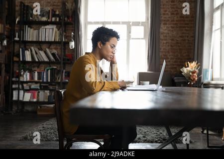 Seriöse afrikanische Frau starrt auf den Laptop-Bildschirm, Seitenansicht Stockfoto