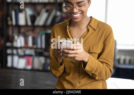 Lächelnde afrikanische Frau in Brille benutzen Handy, beschnittene Ansicht Stockfoto