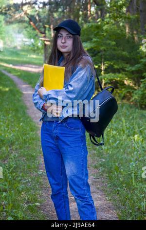 Junge Studentin mit blauen Augen, Ordner und Rucksack auf Naturhintergrund. Stockfoto