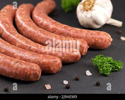 Rohe Kalbswürste mit Petersilie, Knoblauch und Gewürzen auf schwarzem Schiefer, Nahaufnahme von leckeren roten Würsten bereit zum Grillen Stockfoto