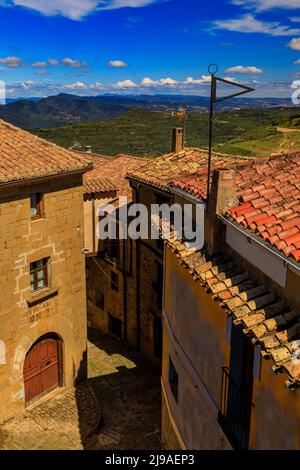 Luftaufnahme von alten Terrakotta-Dächern und terrassenförmigen Feldern, die ein Tal bei der Festungskirche Iglesia de Santa Maria in Ujue, Navarra, Spanien, umgeben Stockfoto