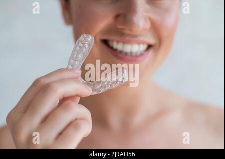 Nahaufnahme eines kieferorthopädischen Silikon-Transparent-Zahnausrichters in den weiblichen Händen. Nicht erkennbare Frau mit abnehmbarem Nachtbügel. Zahnhalterung Stockfoto