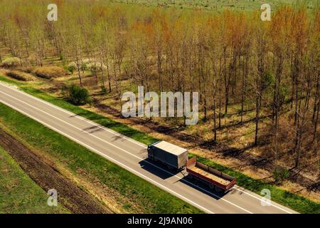 Luftaufnahme eines Sattelwagens mit einem zweiten Anhänger, der am sonnigen Frühlingstag auf der Autobahn durch bewaldete Landschaft fährt, Drohne pov Stockfoto