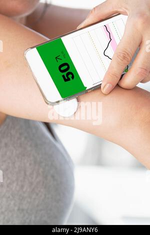 Frau, die den Blutzuckerspiegel mit einem modernen Fernsensor und einem Mobiltelefon ohne Blut überprüft. Konzept der Glukosesensorik für Diabetiker. Wählen Sie Stockfoto