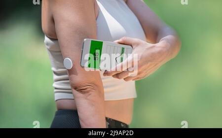 Unkenntliche Frau, die den Blutzuckerspiegel mit einem modernen Fernsensor und einem Mobiltelefon ohne Blut überprüft. Konzept des Glukosesensorgerätes di Stockfoto