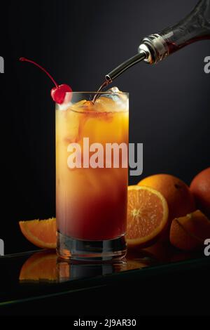 Tequila Sunrise alkoholischer Cocktail in einem hohen Glas. Grenadine wird in ein Glas gegossen. Stockfoto