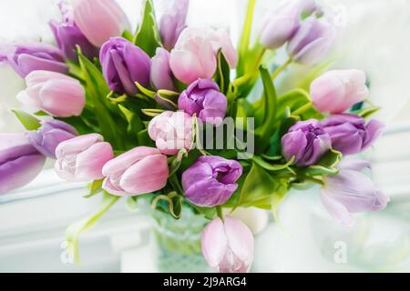 Bunte Tulpen stehen in einer Glasvase auf dem Fenster. Stockfoto