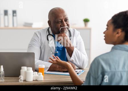 Reife schwarze Arzt hören junge weibliche Patientin Stockfoto