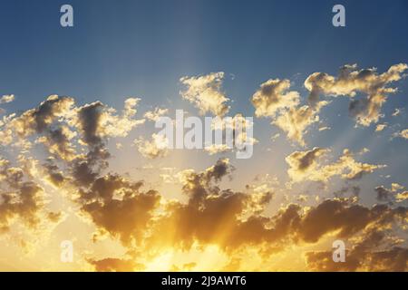 An einem warmen Sommertag strahlen Sonnenuntergänge durch verstreute Kumuluswolken Stockfoto