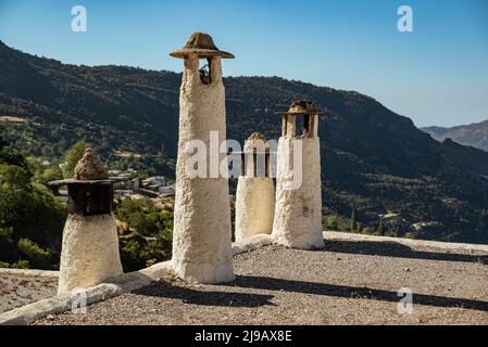 Typische Kamine auf einem Dach in Capileira, mit dem Poqueira-Tal im Hintergrund, Las Alpujarras, Nationalpark Sierra Nevada, Andalusien, Spanien Stockfoto