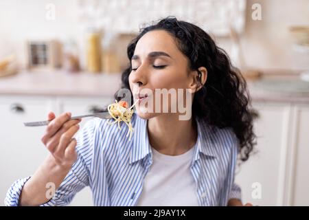 Leckeres Essen. Hungrige junge Frau, die leckere einheimische Spaghetti isst und am Tisch in der Küche sitzt Stockfoto