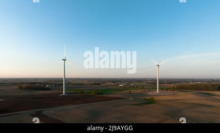 Ein Paar Windturbinen sind in einer ländlichen Landschaft zu sehen, am späten Nachmittag des klaren Himmels. Stockfoto