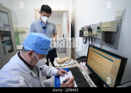 (220522) -- PEKING, 22. Mai 2022 (Xinhua) -- Mei Xiaodong (zurück) wartet darauf, dass der Arzt den Bewohnern unter Hausquarantäne im Chaoyang Bezirk in Peking, der Hauptstadt Chinas, Medikamente verschreibt, 21. Mai 2022. Mei Xiaodong, 35, ist Regierungsangestellter des Bezirks Chaoyang in Peking. Mei wurde entsandt, um sich der Arbeit des Frontpersonals in einer Gemeinde im Kampf gegen COVID-19 anzuschließen und den Bewohnern unter Quarantäne zu helfen, Medikamente für chronische Krankheiten zu kaufen. Gemeindemitarbeiter, Ärzte und Freiwillige tragen die Verantwortung für die Bewertung, den Kauf und die Lieferung von Medikamenten, die von RE bestellt wurden Stockfoto