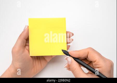 Haftnotizpapier zum Nachbau. Handgeschriebene Notizen schwarzer Bleistift auf gelbem Aufkleber. Weißer Tischhintergrund. Frau handschriftlich auf gelben Haftnotizen. Weiblich Stockfoto