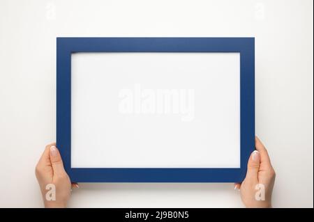 Nachbau des Haltrahmens. Foto-Mockup. Frau Hände halten blauen Rahmen. Für Rahmen- und Poster-Design. Rahmengröße A4. Isoliert auf weißem Hintergrund. Blank pho Stockfoto