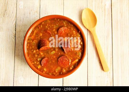 Tonschüssel mit Linsensuppe mit spanischer Wurst oder Chorizo mit Holzlöffel neben der Schüssel, traditionelles spanisches Essen. Foto isolieren Stockfoto
